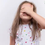 Fetita care isi acopera ochii cu palma